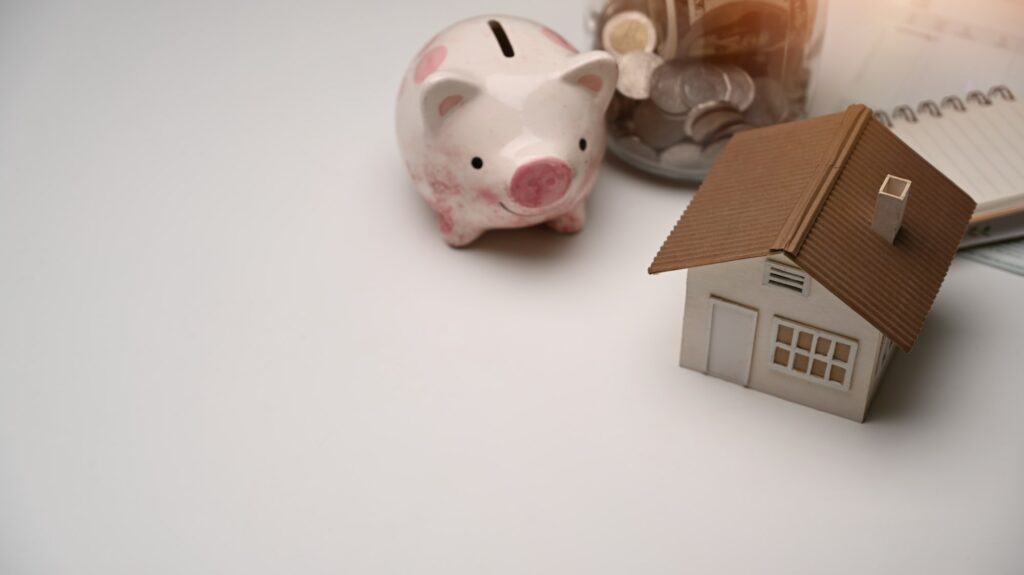 Piggy bank, coin and house model on white table. Save money for future.