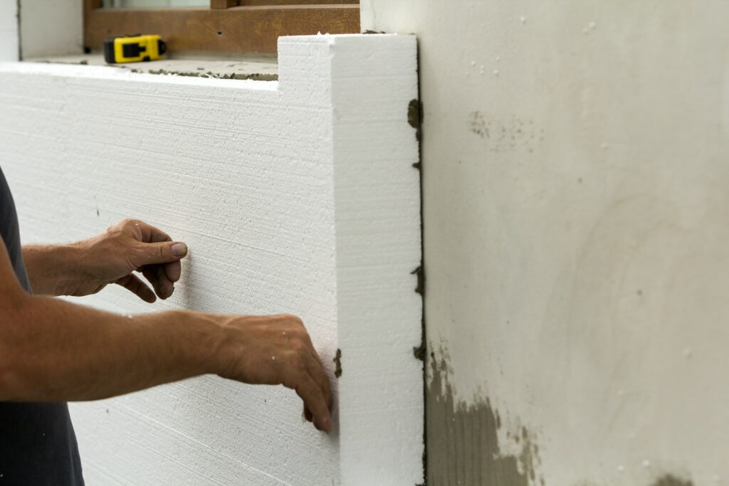 Worker hands installing white rigid polyurethane foam sheet on plastered brick wall. Modern